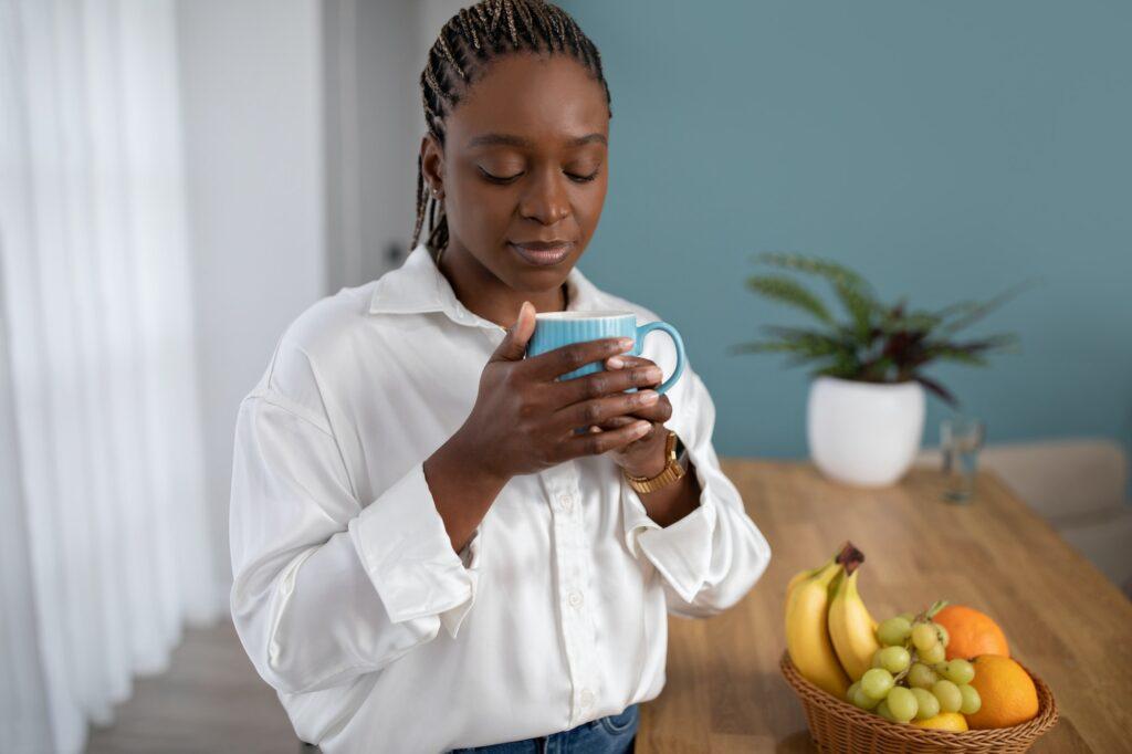 Peaceful young black woman drinking coffee at home